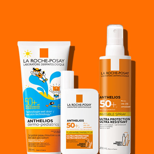 Three La Roche-Posay Anthelios sunscreen products are displayed against a bright orange background. The products include a tube of children's sunscreen lotion, a small bottle of sunscreen for facial use, and a spray sunscreen, all labeled with SPF 50+.