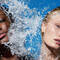 A close-up of two models with different skin tones, surrounded by splashing water against a bright blue background. The mood is fresh and summery.