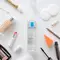 A clear bottle of La Roche-Posay micellar water surrounded by various makeup products, including a foundation, lipstick, lip pencil, and a cosmetic sponge.