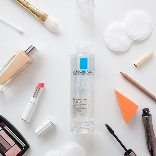 A bottle of La Roche-Posay micellar water placed among various beauty products, including a lipstick, foundation, and a makeup pencil.