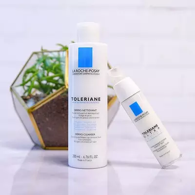 A close-up of La Roche-Posay Toleriane skincare products, featuring a cleanser and moisturizer, placed next to a small green plant in a decorative container.