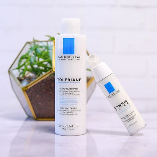 A flat lay of two La Roche-Posay Toleriane skincare products: a cleanser and a moisturizer, displayed next to a small potted plant in a geometric pot.