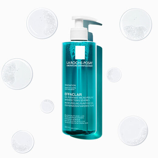 A bottle of La Roche-Posay Effaclar purifying gel, surrounded by small droplets of the product, with a clear background.