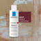 A bottle of La Roche-Posay Kerium DS deep scalp cleansing shampoo with a textured background. The label emphasizes its purpose for treating persistent dandruff.