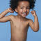 A joyful child with curly hair smiles widely, showcasing their teeth against a light blue background.