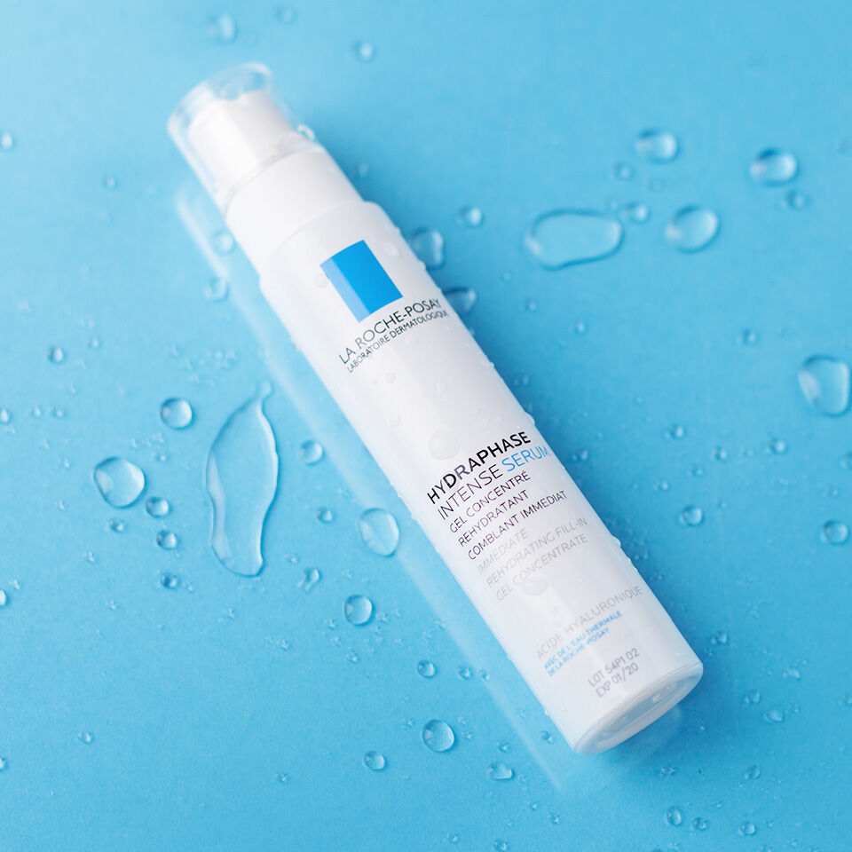 A bottle of La Roche-Posay Hydraphase Intense Serum is placed on a blue surface with water droplets around it.