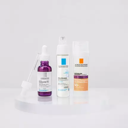 Three skincare products displayed on a circular pedestal: a dark purple serum with a dropper, a white moisturizer in a pump bottle, and a light orange sunscreen in a cream tube. All products are from the La Roche-Posay brand.