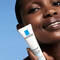 A close-up of a person holding a tube of La Roche-Posay Effaclar Duo+ skin treatment, against a blue background.