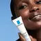 A close-up of a person holding a tube of La Roche-Posay Effaclar Duo+ skin treatment, against a blue background.