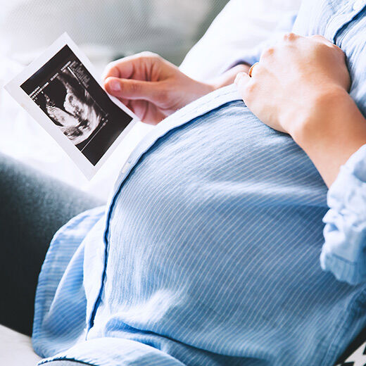 A pregnant person holding an ultrasound image while gently resting their hand on their belly.