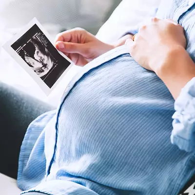 A pregnant person holding an ultrasound image while gently resting their hand on their belly.