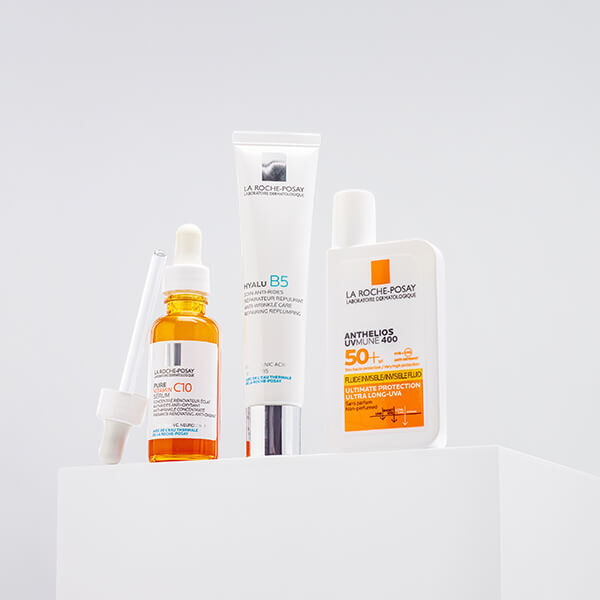 Four skincare products displayed on a white pedestal, including a serum with a dropper, a cream labeled "Hyalu B5," and a sunscreen labeled "Anthelios."