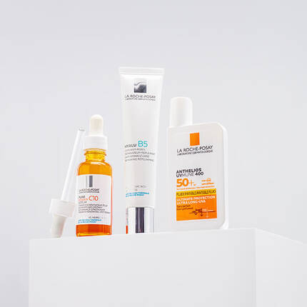 Four skincare products displayed on a white pedestal, including a serum with a dropper, a cream labeled "Hyalu B5," and a sunscreen labeled "Anthelios."
