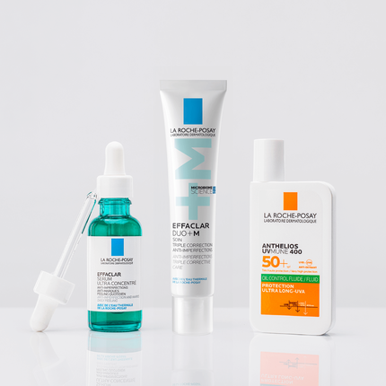 Three skincare products displayed on a neutral background: a blue serum with a dropper, a white tube of cream, and an orange bottle of sunscreen.