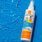 A bottle of La Roche-Posay Anthelios SPF 50+ sunscreen for children resting on the surface of a sparkling blue swimming pool.