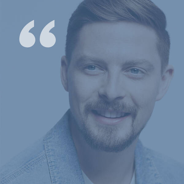 A smiling young man with short hair and a beard, wearing a denim jacket, against a light blue background with quotation marks above his head.