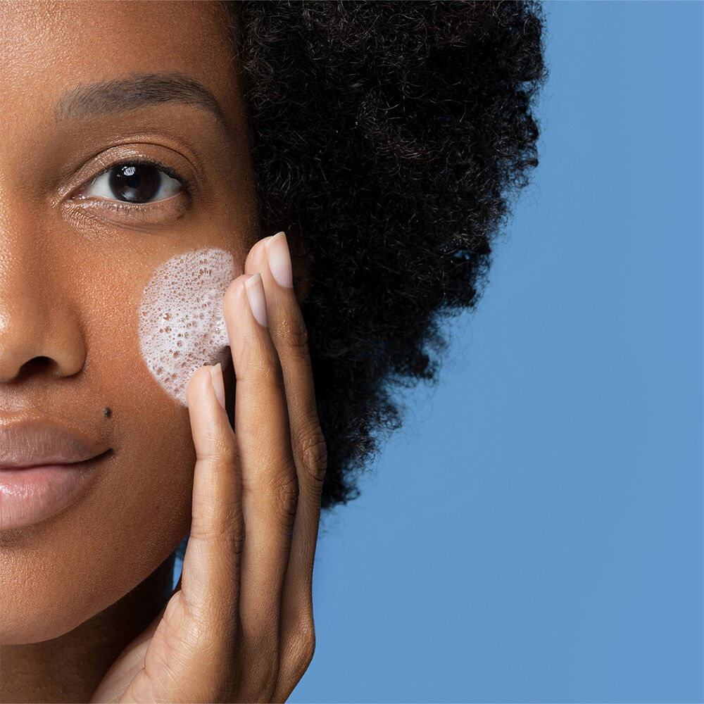 Woman gently massages a cleanser onto her cheek, creating a lather
