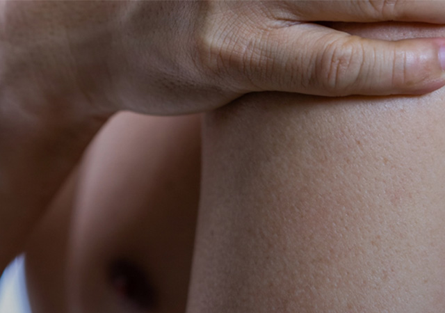 A close-up of a person's bare shoulder and arm, with one hand gently resting on the shoulder. The skin appears smooth and the background is softly blurred.