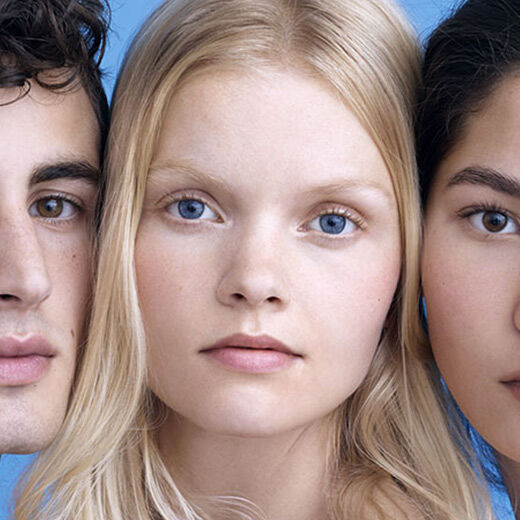 A close-up portrait of three individuals with various features, arranged side by side against a light blue background. They have neutral expressions and are looking directly at the camera, showcasing their diverse appearances.