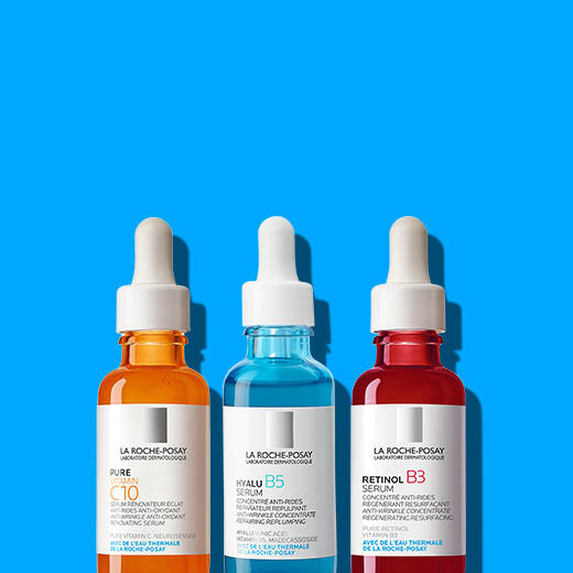 Three serum bottles from La Roche-Posay in front of a bright blue background. The bottles are labeled as Pure C10, Hyalu B5, and Retinol B3. Each has a dropper cap.