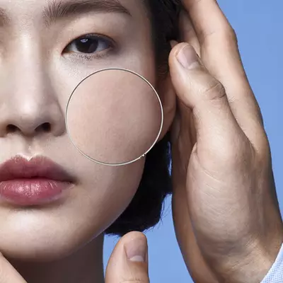 Close-up of a person’s face with a hand holding a magnifying glass, showcasing the skin's texture against a blue background.