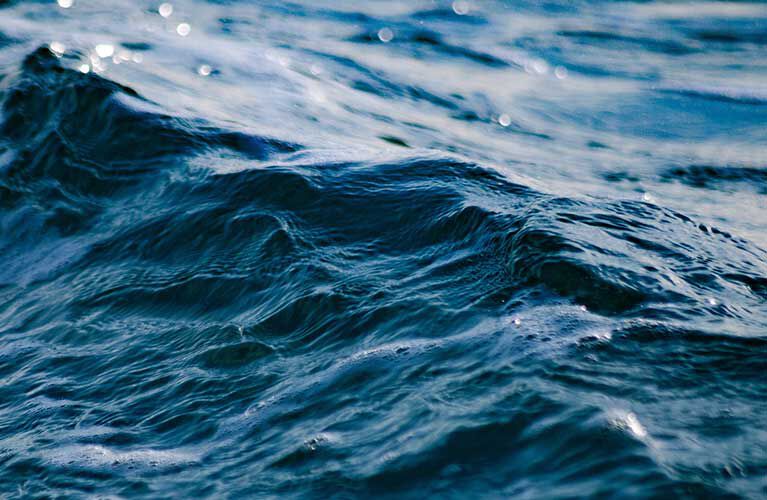 Close-up of gently rolling ocean waves with subtle reflections of light creating a shimmering effect on the water's surface.