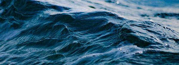 Close-up of gently rolling ocean waves with subtle reflections of light creating a shimmering effect on the water's surface.