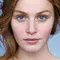 A close-up of a person's face, focusing on their striking blue eyes and reddish-brown eyebrows, with a soft, natural expression.
