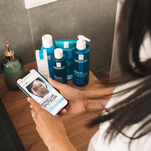 A person holding a smartphone displaying a skincare analysis app, surrounded by various La Roche-Posay skincare products.