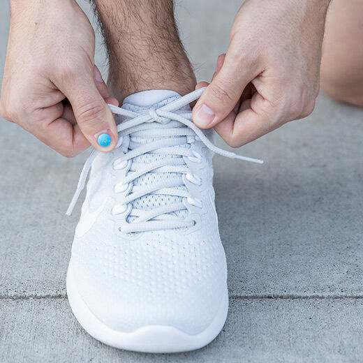 A close-up of hands tying the laces of a white sneaker on a concrete surface.