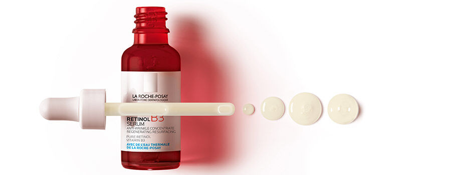 Four colorful serum bottles in various shapes, featuring labels that indicate their active ingredients, displayed against a white background. The bottles are purple, blue, orange, and clear.