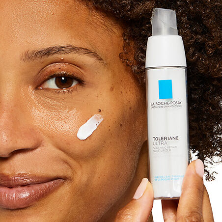Woman smiling with a swatch of Toleriane Ultra moisturiser on her cheek, whilst holding the product up to her face