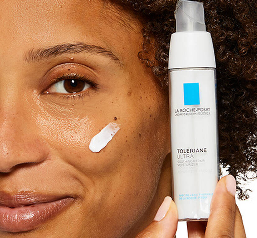 Woman smiling with a swatch of Toleriane Ultra moisturiser on her cheek, whilst holding the product up to her face