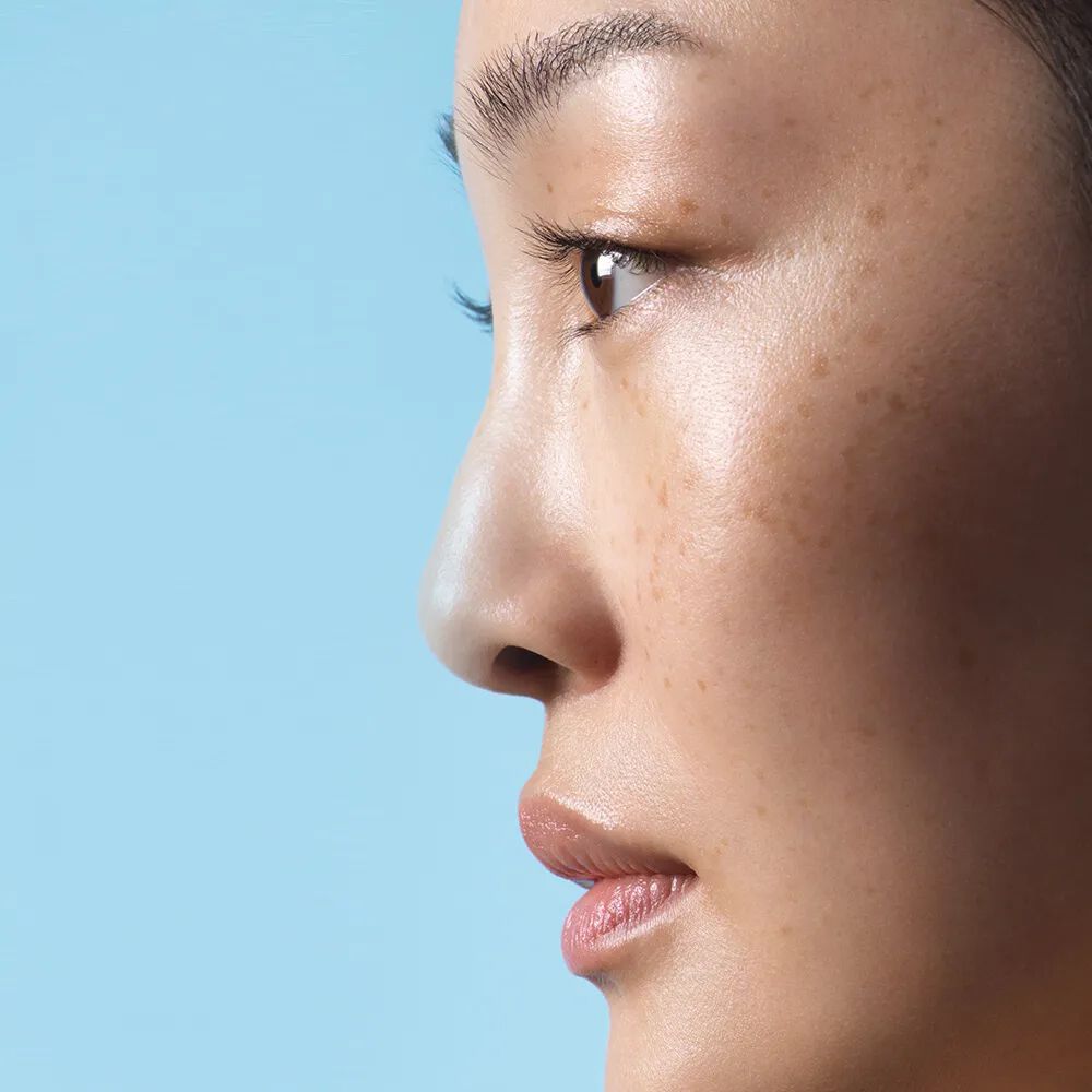 A close-up profile of a woman with smooth skin and subtle makeup, against a light blue background.