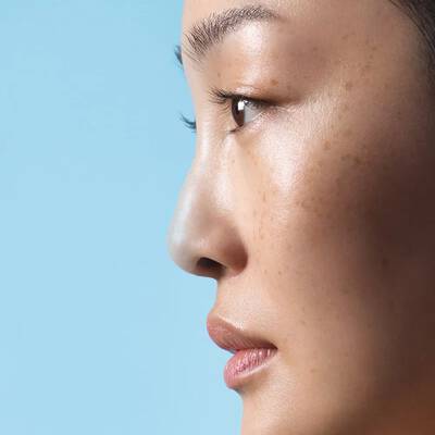 A close-up profile of a woman with smooth skin and subtle makeup, against a light blue background.