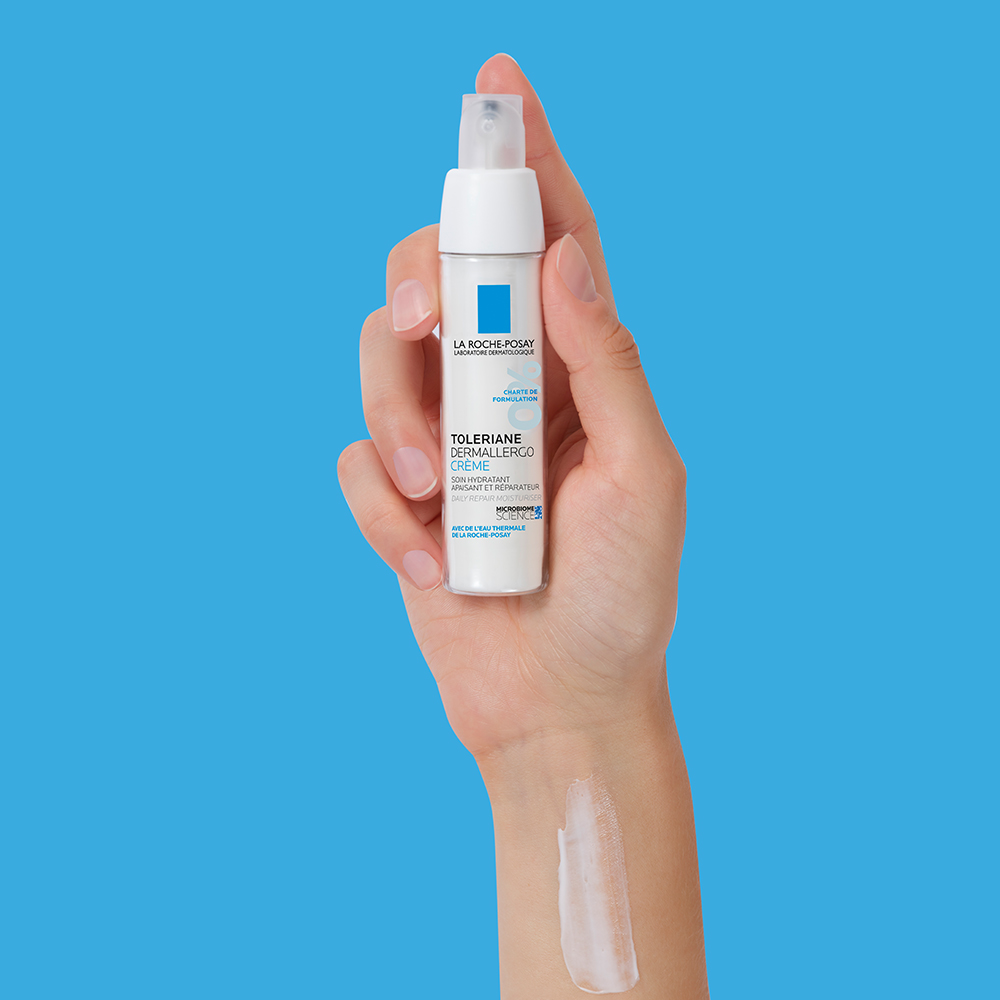 A hand holding up Toleriane Dermallergo Cream, with a swatch of the product on her wrist
