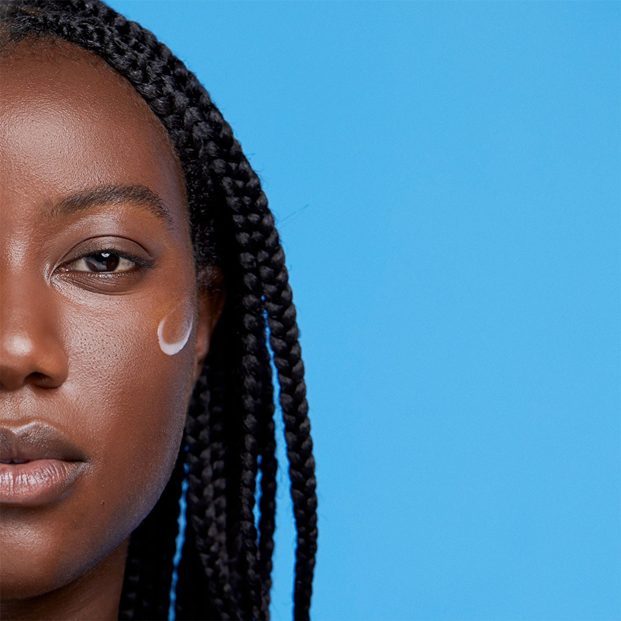 Close-up of a woman with braided hair and a streak of moisturiser on her cheek.